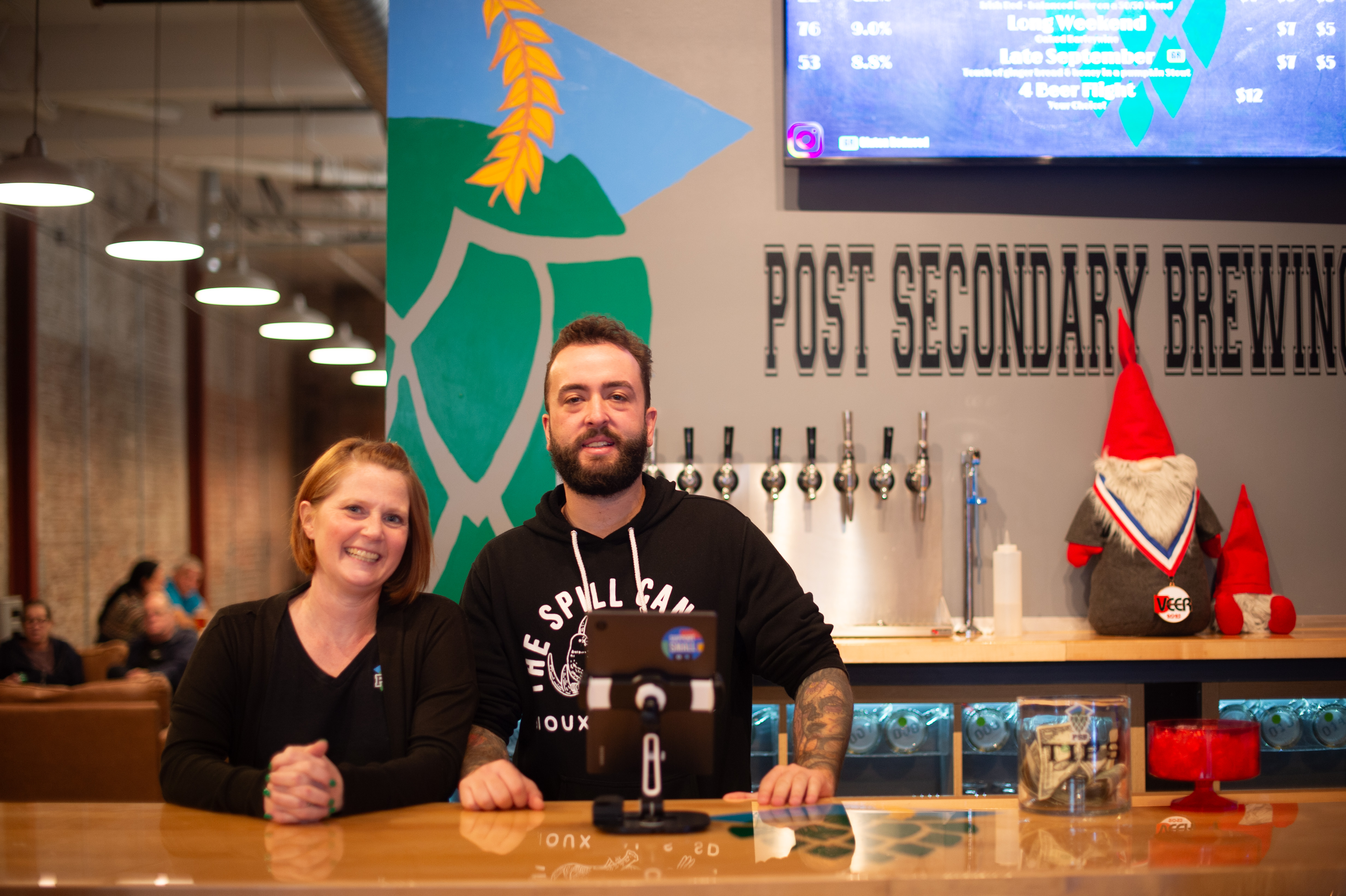 Post Secondary Brewing owner and employee standing behind their bar and smiling